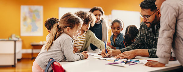 children in class watching male teacher grade papers